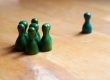 Eine einzelne grün-blaue Spielfigur steht abseits von einer Gruppe grüner Figuren. Das Bild verdeutlicht Ausgrenzung, soziale Isolation und Formen der Diskriminierung.
