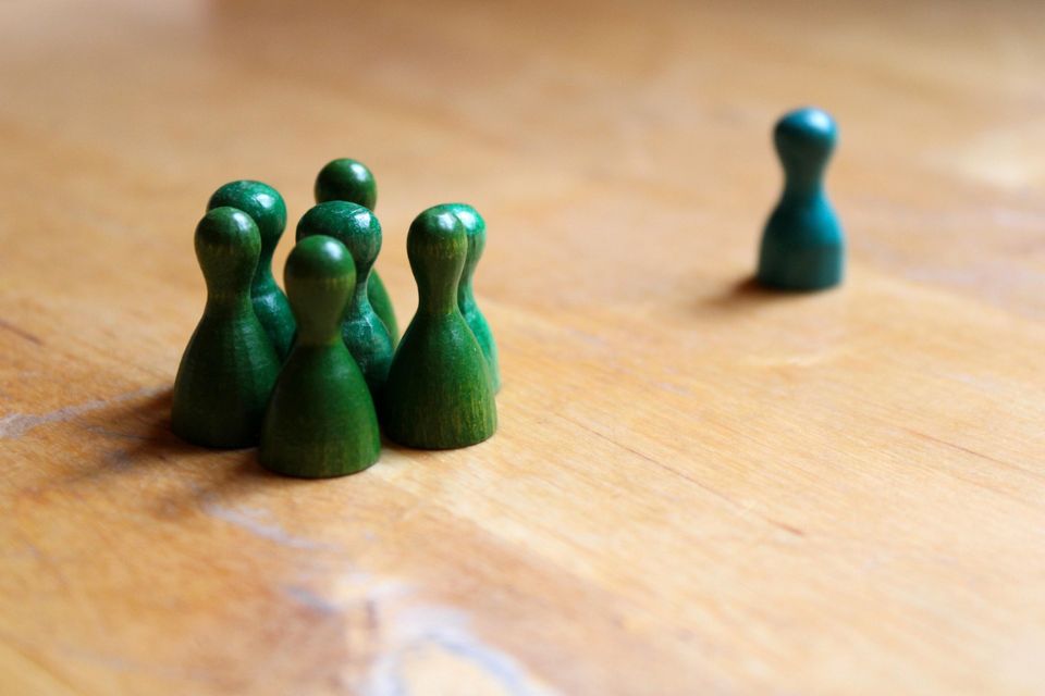 Mikroaggressionen Eine einzelne grün-blaue Spielfigur steht abseits von einer Gruppe grüner Figuren. Das Bild verdeutlicht Ausgrenzung, soziale Isolation und Formen der Diskriminierung.