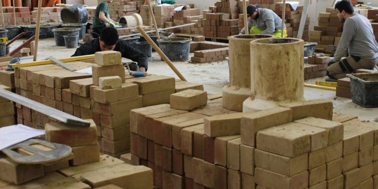 Studie Fachkräfte Vier Personen lernen in einer Werkstatt Bauarbeiten. Sie arbeiten mit Ziegeln und verschiedenen Werkzeugen.