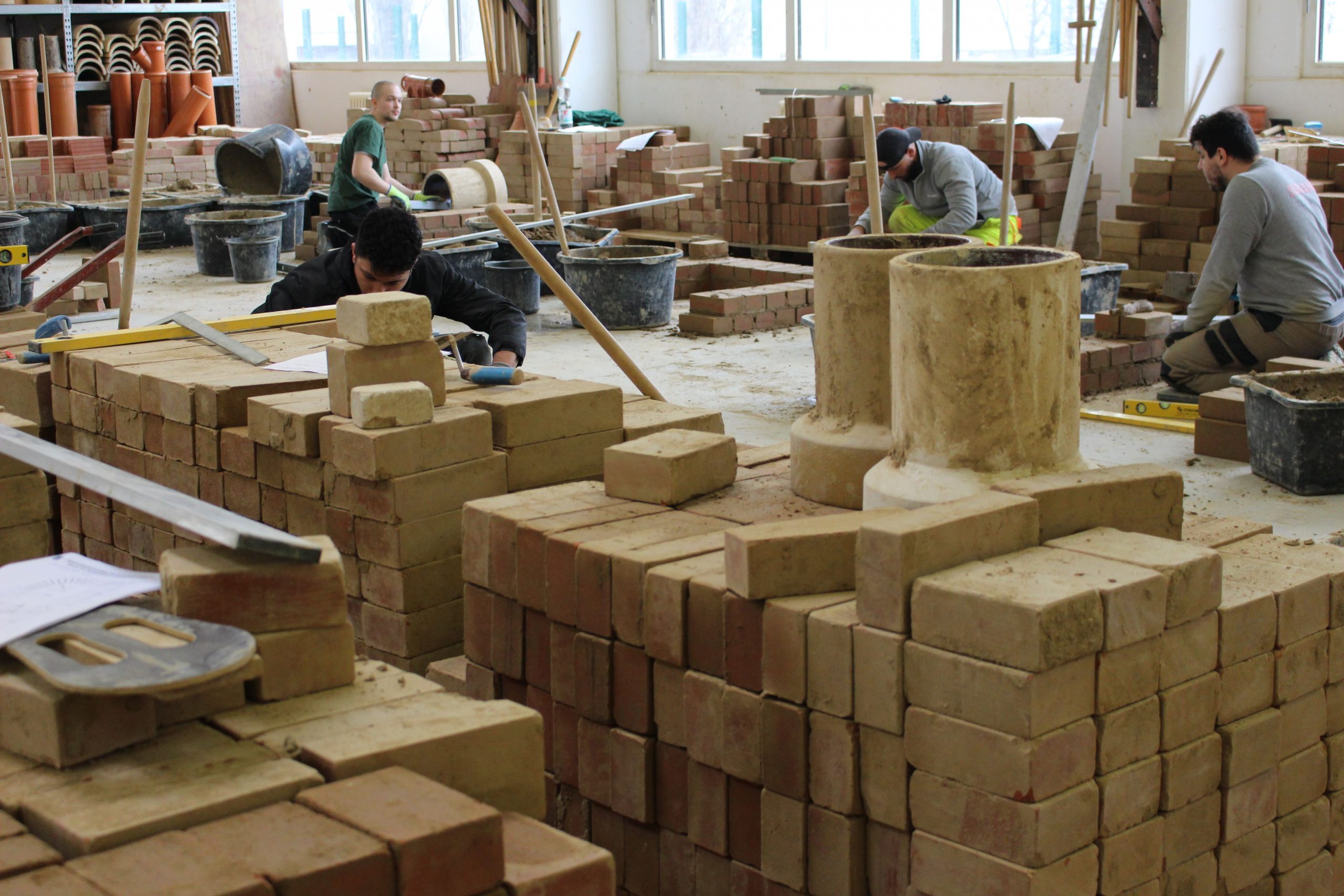 Studie Fachkräfte Vier Personen lernen in einer Werkstatt Bauarbeiten. Sie arbeiten mit Ziegeln und verschiedenen Werkzeugen.