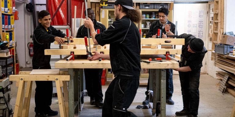 200708_ARRIVO_Tischbau_LUIS-KRUMMENACHER_web-1034264 Fünf Personen lernen und arbeiten gemeinsam in einer Holzwerkstatt mit Werkzeugen in einer angenehmen Umgebung.