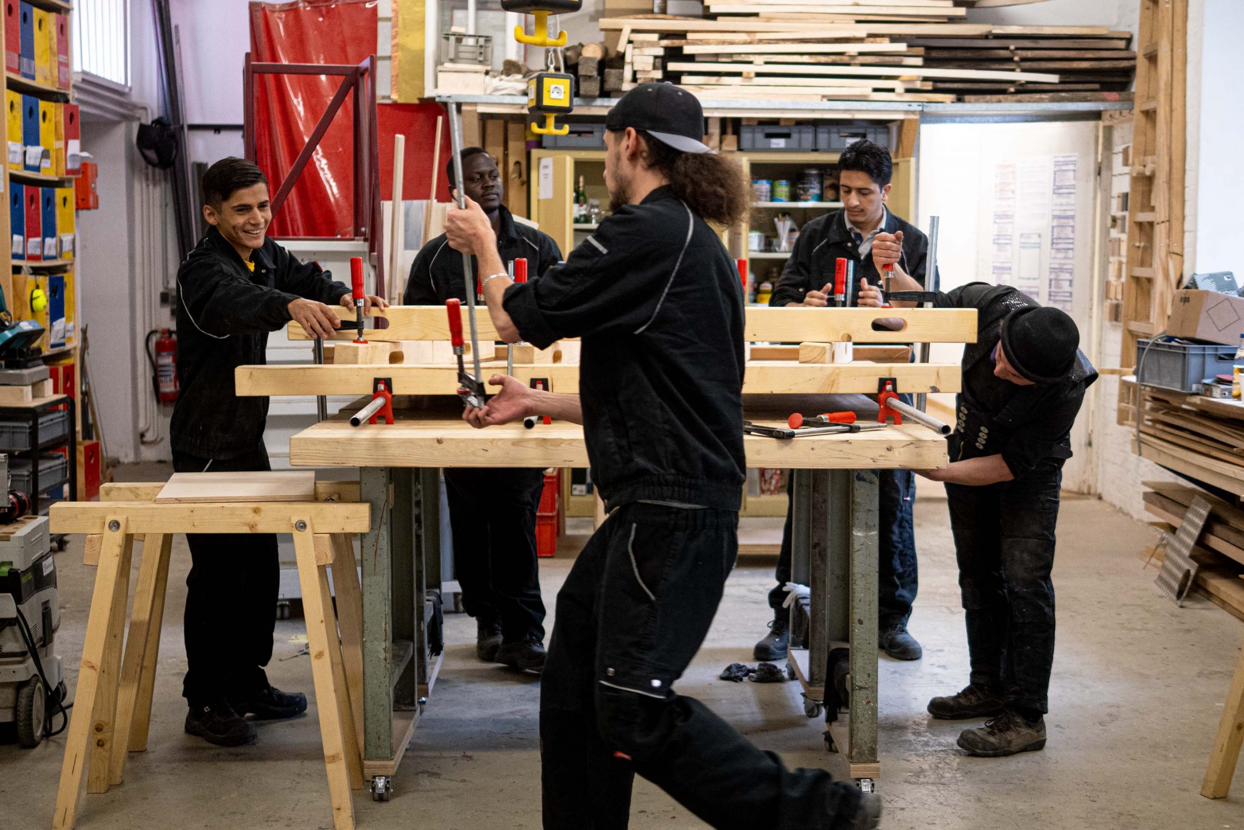 Fünf Personen lernen und arbeiten gemeinsam in einer Holzwerkstatt mit Werkzeugen in einer angenehmen Umgebung.