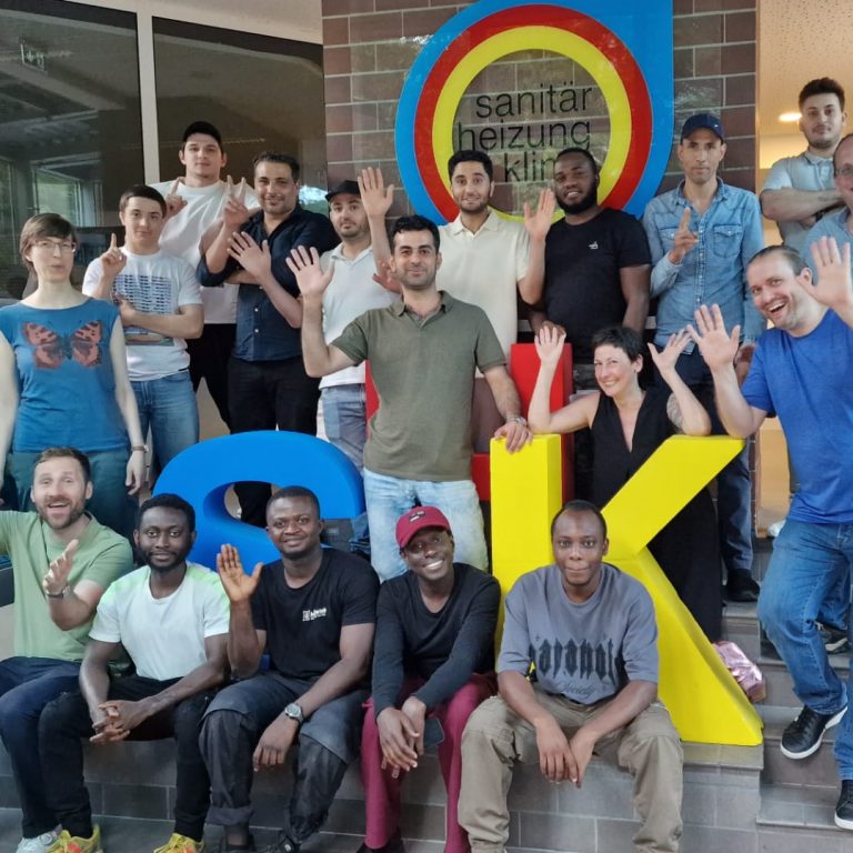 Eine Gruppe von 18 Personen – Teilnehmende des Projekts sowie das Coaching- und Beratungsteam – steht lächelnd vor der Kamera. Im Hintergrund ist das Logo der Innung SHK Berlin zu sehen